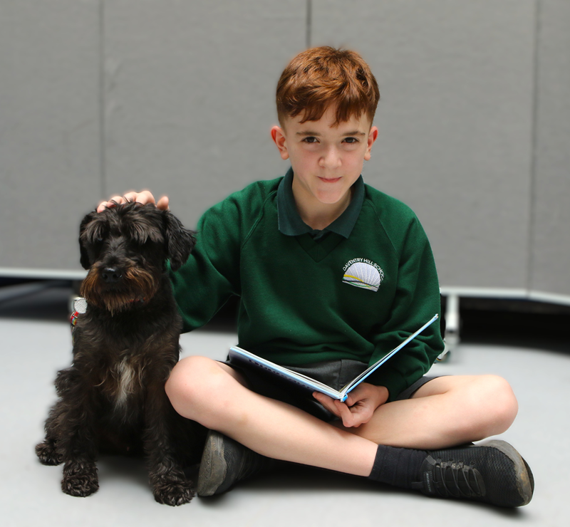 Boy with school dog Raffie reading a book at Daventry Hill School